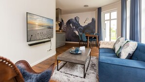 Ein Wohnzimmer mit einem blauen Sofa, einem Couchtisch und einem Gemälde von einem Sonnenuntergang.