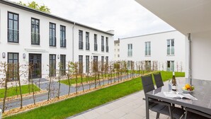 A modern building with a patio area featuring a table with chairs, a bottle, and a bowl of fruit. - Quartier am Kurpark, app. 02 (Heringsdorf)