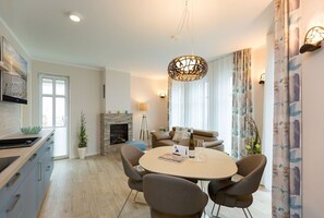 Uma sala de jantar moderna com uma mesa redonda, cadeiras, um candelabro, lareira e um sofá.