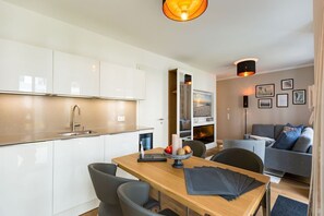 Une cuisine moderne avec des meubles blancs, une table à manger avec des chaises et un coin salon avec un canapé et une cheminée.