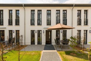 Un bâtiment moderne doté d’une entrée centrale, d’un espace extérieur abrité avec des sièges et d’un jardin bien entretenu.