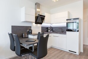 Une cuisine moderne avec des meubles blancs, un four encastré et un coin repas comprenant une table et des chaises.