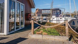 A waterfront property with a wooden exterior, large windows, and a view of boats docked in the background. - House by Uitgeestermeer with Garden (Uitgeest)