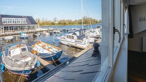 A marina with various boats docked, a building with large windows, and a clear sky. - House by Uitgeestermeer with Garden (Uitgeest)