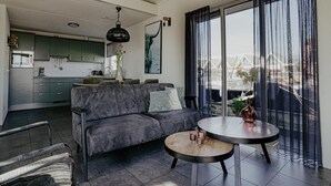 A modern living room with a grey sofa, a round coffee table, and a view of a marina through large windows. - House by Uitgeestermeer with Garden (Uitgeest)