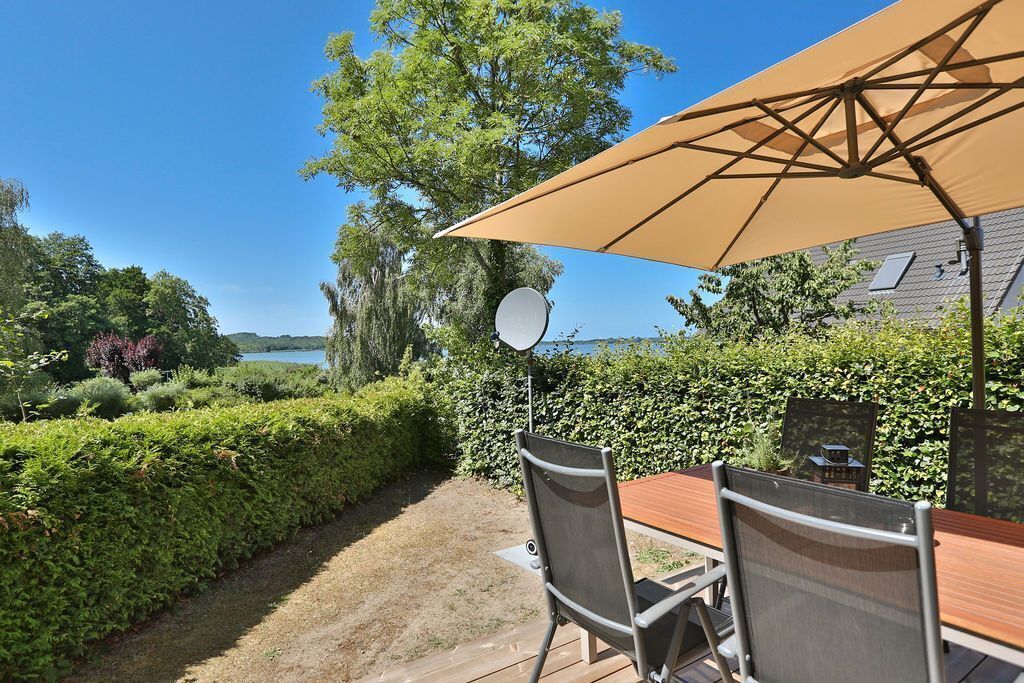 A patio with a table and chairs, a large umbrella, and a view of a lake.