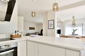 A modern kitchen with white cabinetry, a built-in oven, and pendant lighting. - Vacation cottage Hygge Hus (Sellin/Usedom)