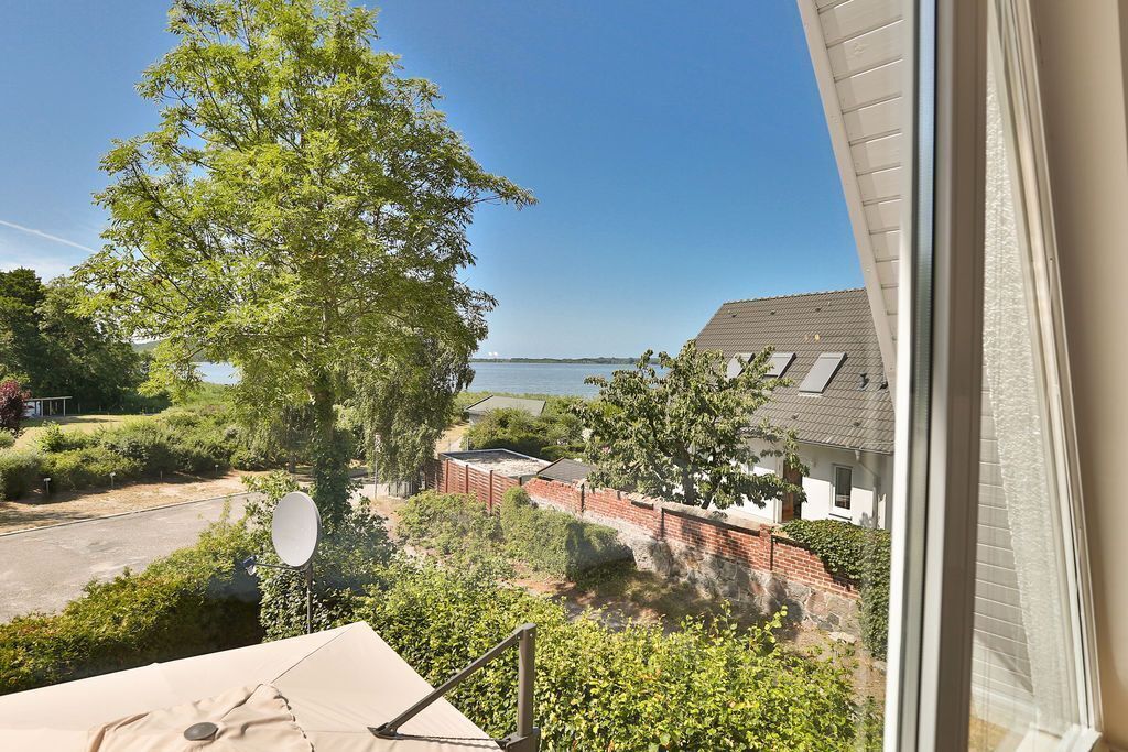Blick aus einem Fenster auf ein Wohngebiet mit einem Haus, einer Satellitenschüssel und einem großen Baum.