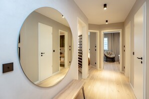 Um corredor moderno com um espelho grande, soalho em madeira e um espaço de estar com uma poltrona acolchoada.