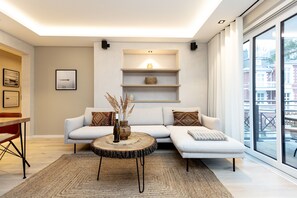 A modern living room with a sectional sofa, a round coffee table, and a large window offering a view of the city.