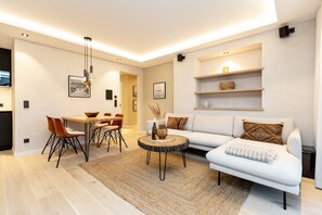 Uma sala de estar moderna com área de jantar, apresentando um sofá branco, uma mesa de centro redonda e uma mesa de jantar com cadeiras.