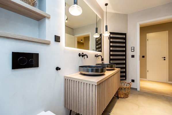 A modern bathroom with a wooden vanity, two sinks, a large mirror, and pendant lighting.