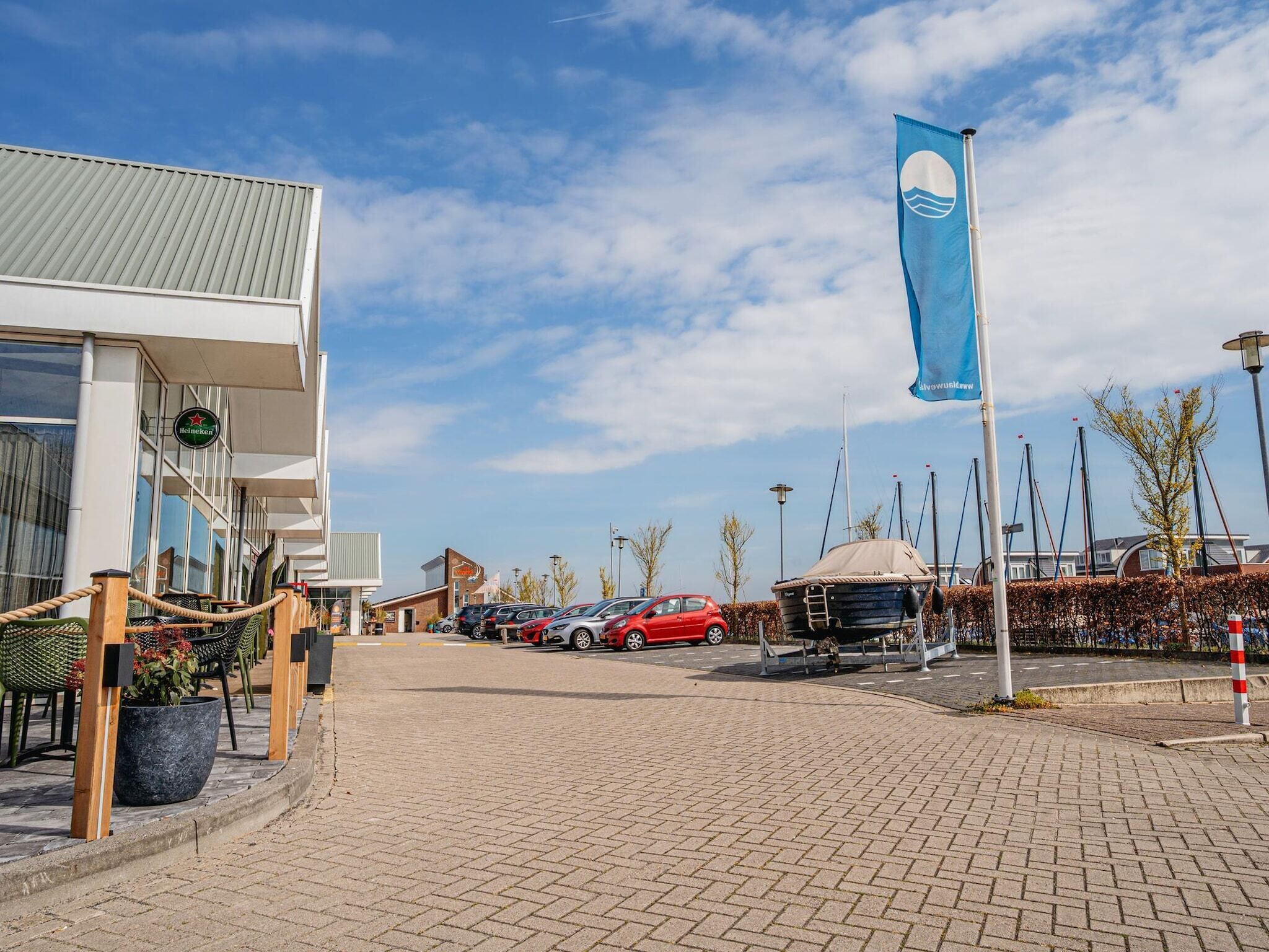 A waterfront building with a Heineken sign, a blue flag, and a row of parked cars.