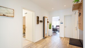 Een hal met houten vloer, witte wanden en een bankje. Er zijn deuren naar andere kamers, een spiegel en een potplant.