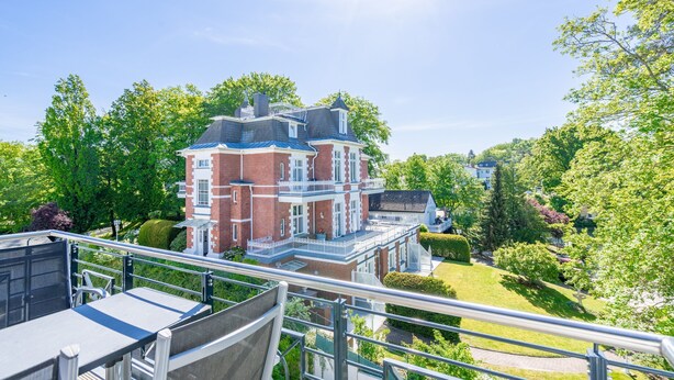Een groot, meerijverig gebouw met een bakstenen gevel en witte decoratielijsten, omringd door weelderige begroeiing en bomen.