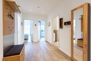 Un couloir doté d’un plancher en bois, d’un banc, d’un miroir et d’une porte donnant sur une cuisine.