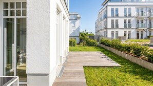 Un bâtiment moderne doté d’une terrasse en bois, d’une pelouse et d’un mur extérieur blanc.