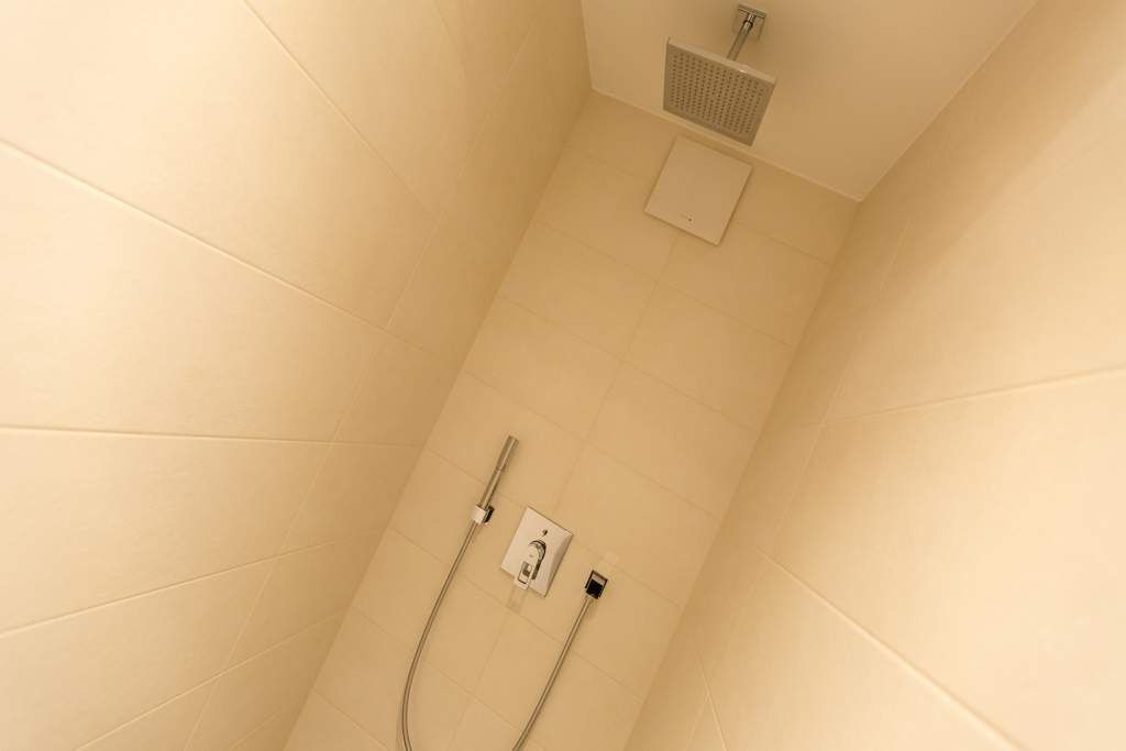 A shower with a handheld showerhead and a wall-mounted control panel.