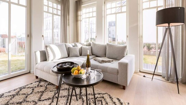 Un salon moderne avec un canapé gris, une table basse ronde sur laquelle on trouve des fruits et une bouteille, et un lampadaire.