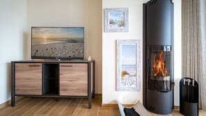 En moderne stue med TV, pejs og indrammede billeder fra stranden på væggen.
