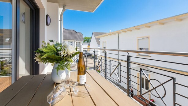 En balkon med et træbord, en vinflaske og en vase med blomster.