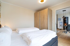 Ein Hotelzimmer mit zwei Betten, einem Holzschrank, einem Glastisch mit Stuhl und einem sichtbaren Kamin.