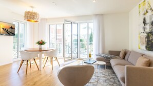 A modern living room with a sofa, a dining table with chairs, and a large window with a view of buildings. - Quartier Eichenweg, app. 3 (Heringsdorf)