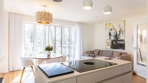 A modern kitchen with a central island, a dining area with a round table and chairs, and a living area with a sofa and a large window. - Quartier Eichenweg, app. 3 (Heringsdorf)