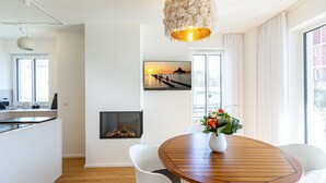 A modern kitchen with white cabinetry, a built-in oven, and a dining area with a wooden table and white chairs. - Quartier Eichenweg, app. 3 (Heringsdorf)