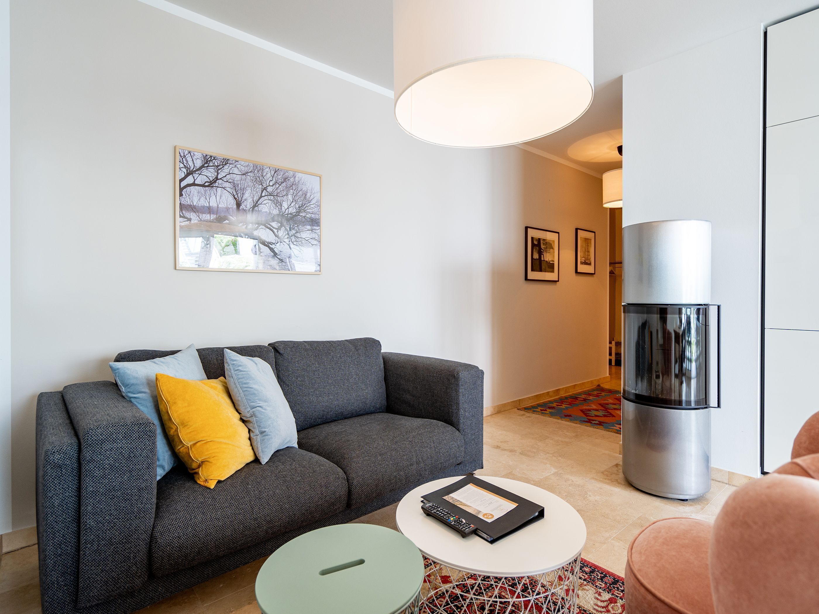 A modern living room with a grey sofa, a small round table, and a large cylindrical appliance, likely a refrigerator or oven, in the background.