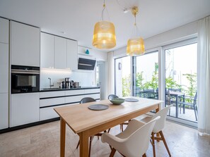 A modern kitchen with white cabinets, a wooden dining table, and two pendant lights. - Quartier 7, App. 01, Germany (Heringsdorf)