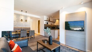 Una sala de estar moderna con sofá, mesa de centro y comedor. Se ve una cocina al fondo, con un amplio ventanal.