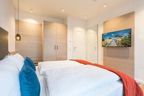 A modern hotel room with a large bed, a TV mounted on the wall, and wooden paneling on the walls. - Beachhouse Bansin, App. 20 (Heringsdorf)