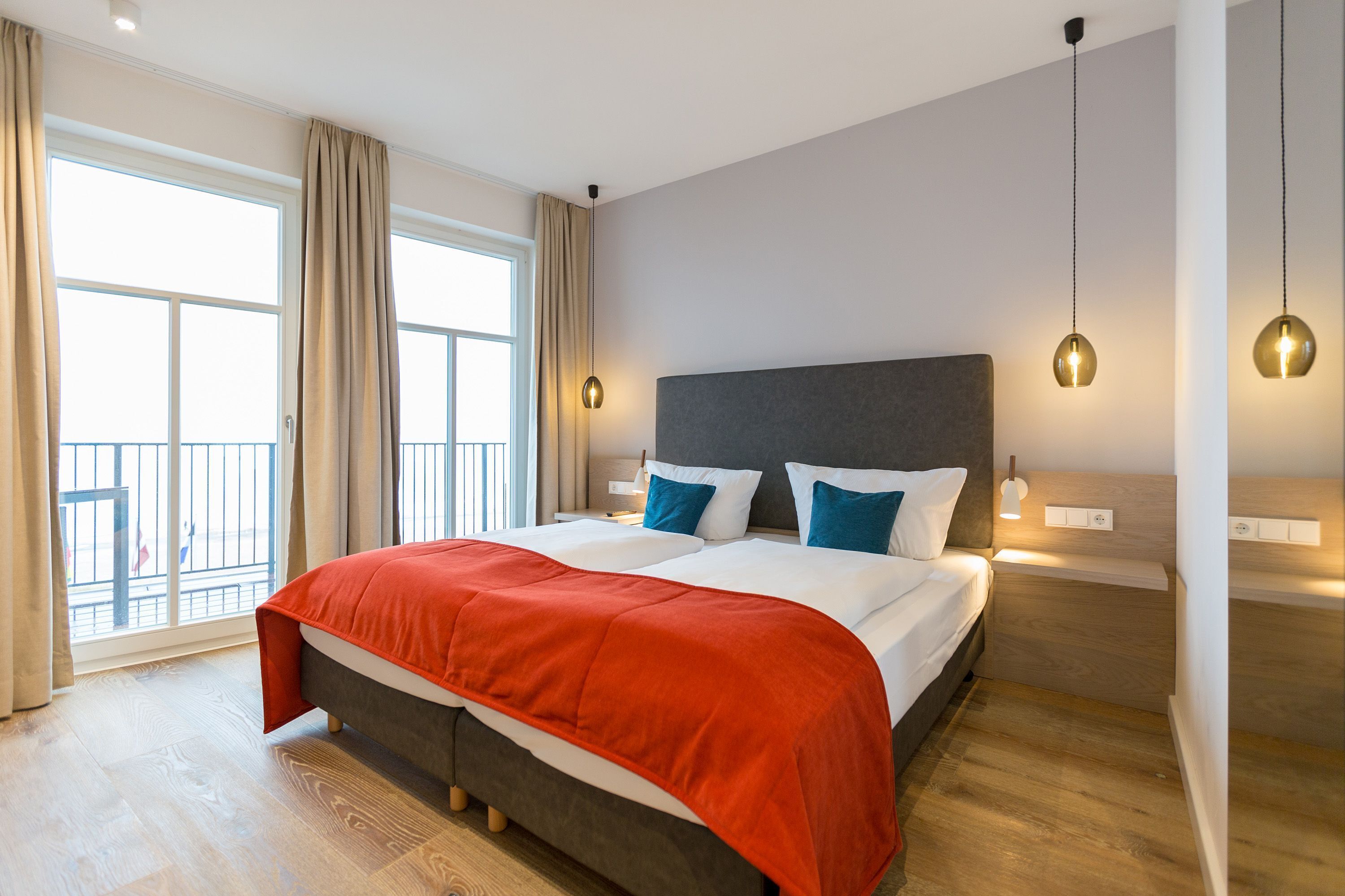 A modern hotel room with a large bed, a balcony view, and pendant lighting.