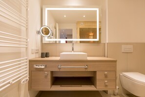 Uma casa de banho moderna com uma pia branca, um espelho com iluminação integrada, um porta-toalhas e uma sanita.