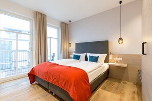 Habitación de hotel moderna con una cama grande, una mesita de noche, una ventana con cortinas y vistas al balcón.