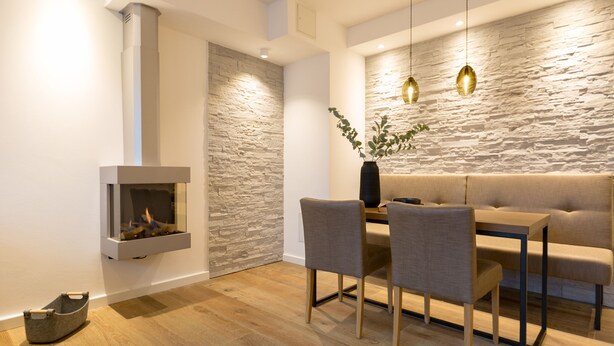 A modern dining area with a stone wall, a built-in fireplace, and a wooden dining table with chairs.