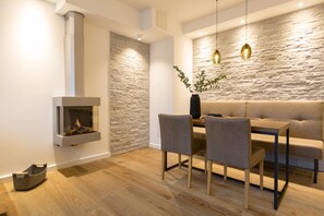 Un espace repas moderne avec un mur en pierre, une cheminée intégrée et une table à manger en bois, accompagnée de chaises.
