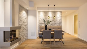 A modern living room with a stone accent wall, a fireplace, a dining area with a sofa and table, and pendant lighting.