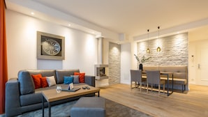 A modern living room with a grey sofa, a wooden coffee table, and a dining area with a stone wall and pendant lights.
