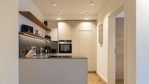 A modern kitchen with a central island, built-in appliances, and wooden shelving.