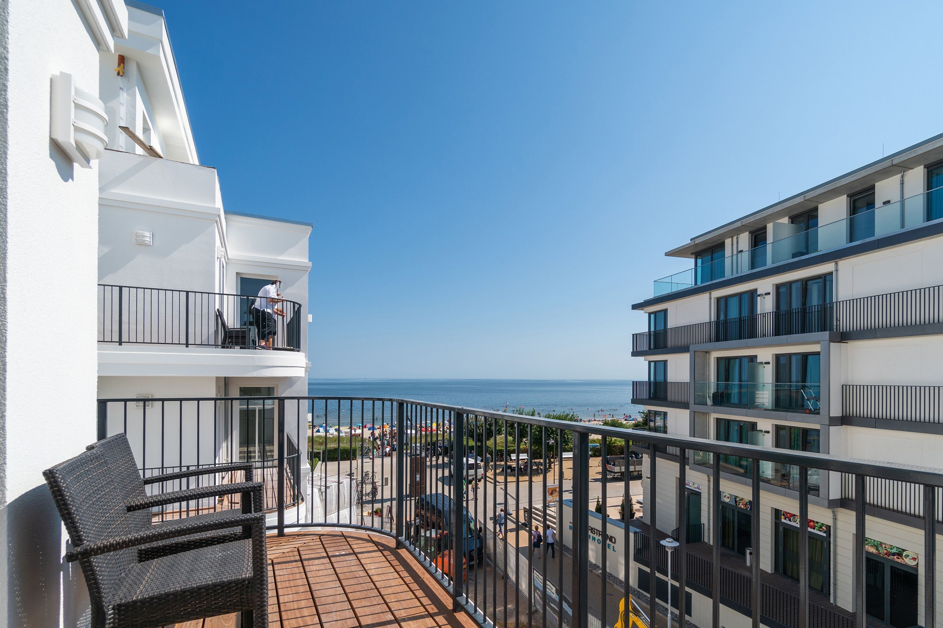 Un balcon doté de meubles en osier, une vue sur la mer et des immeubles modernes situés à proximité.