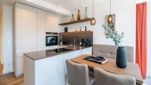 A modern kitchen with a central island, built-in appliances, and a dining area with a table and chairs. - Beachhouse Bansin, app. 22 (Heringsdorf)