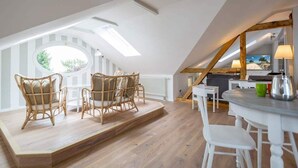 Un dormitorio estilo loft acogedor con techo inclinado, tragaluces, zona de comedor con mobiliario blanco y vistas al exterior.