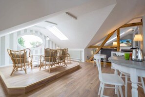 Quarto de loft aconchegante com teto inclinado, claraboia, área de refeições com mobiliário branco e vista para o exterior.