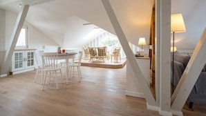 Un loft espacioso con techo alto, un comedor con sillas blancas y una mesa redonda, y una zona de estar acogedora con sofá y lámparas.