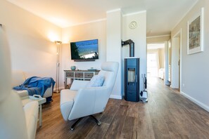 Ett modernt vardagsrum med en platt-TV, en massagefåtölj, en öppen spis och en hall som leder till andra rum.