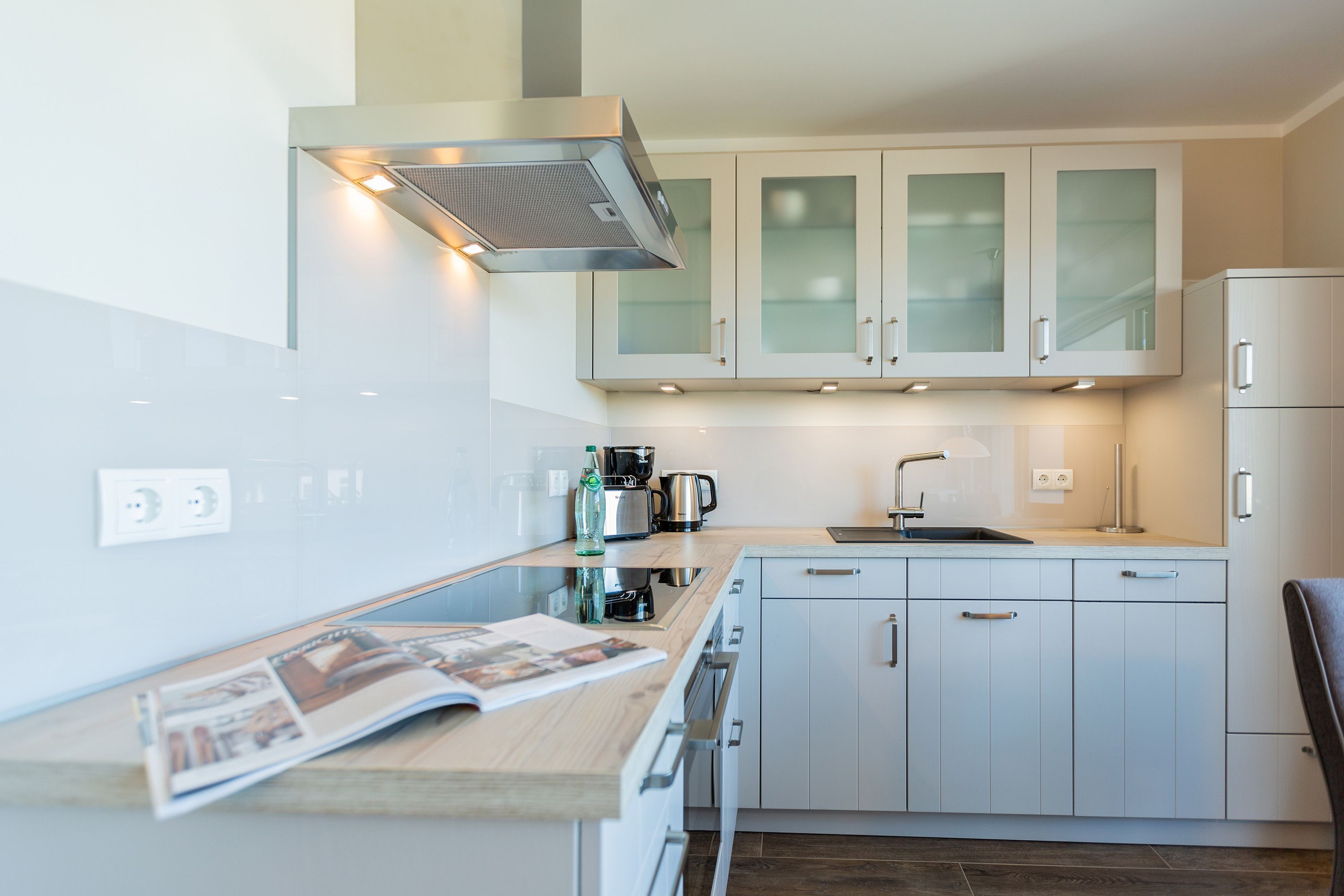 A modern kitchen with white cabinets, a built-in oven, and a coffee maker.