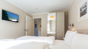 A hotel room with two beds, a TV, a mirror, and a door leading to a bathroom. - Quartier am Fischerstrand, App. 3 (Heringsdorf)