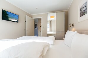 A hotel room with two beds, a TV, a mirror, and a door leading to a bathroom. - Quartier am Fischerstrand, App. 3 (Heringsdorf)